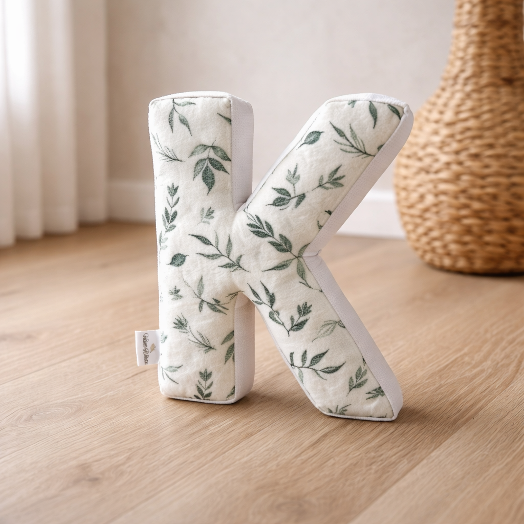 Personalized botanical letter K pillow in neutral nursery setting