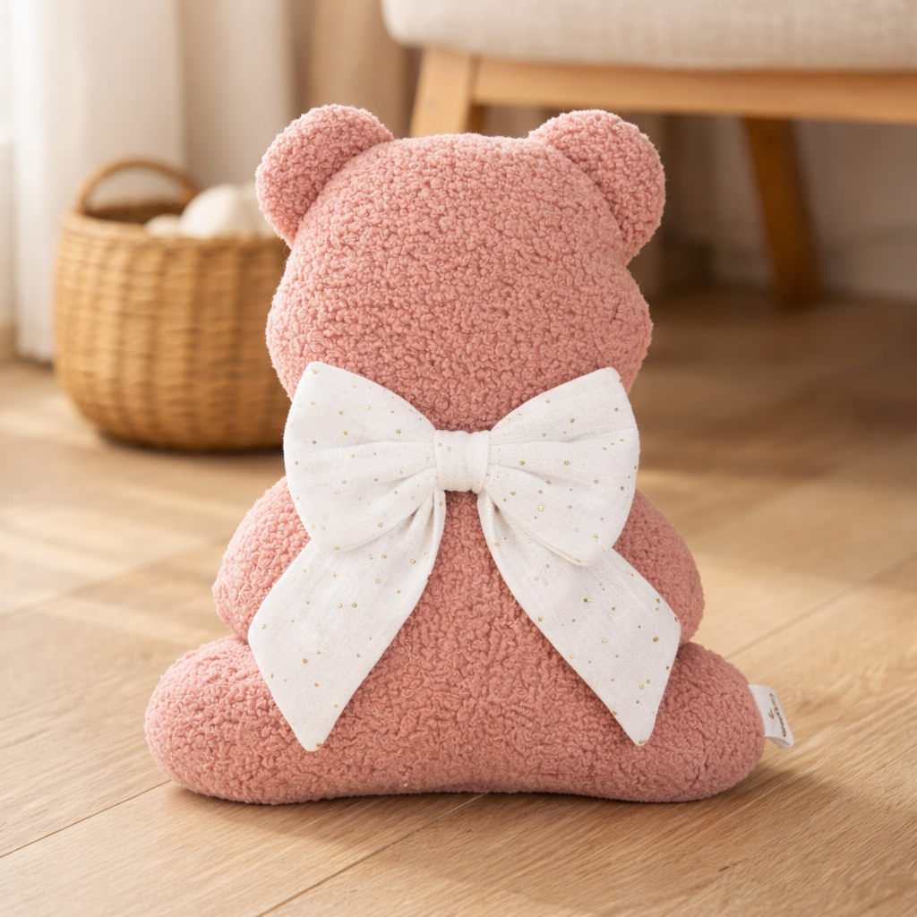 Pink teddy bear with a white bow on a wooden floor