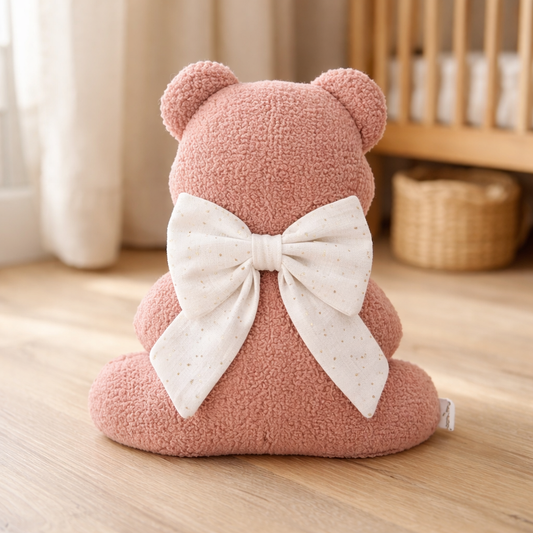 Handmade blush teddy bear pillow with decorative bow in neutral nursery setting