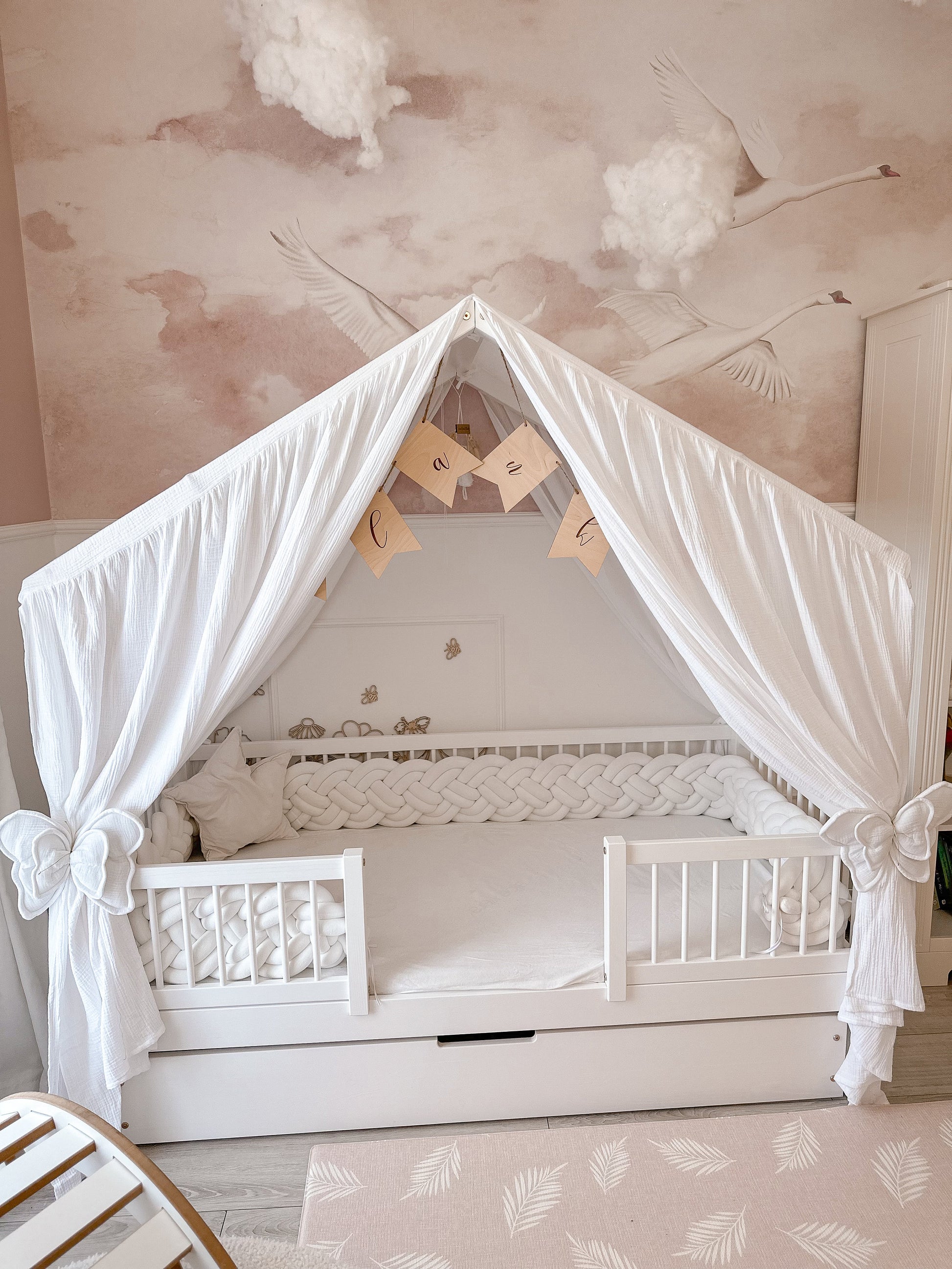 Elegant handmade muslin princess bed canopy in soft pink, draped over a kids’ house bed with fairy lights and pillows.